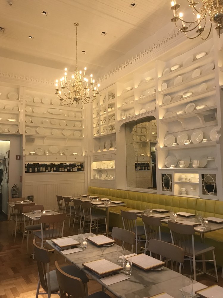 Caffè Storico — yellow banquette beneath the porcelain plate-wall and brass chandeliers