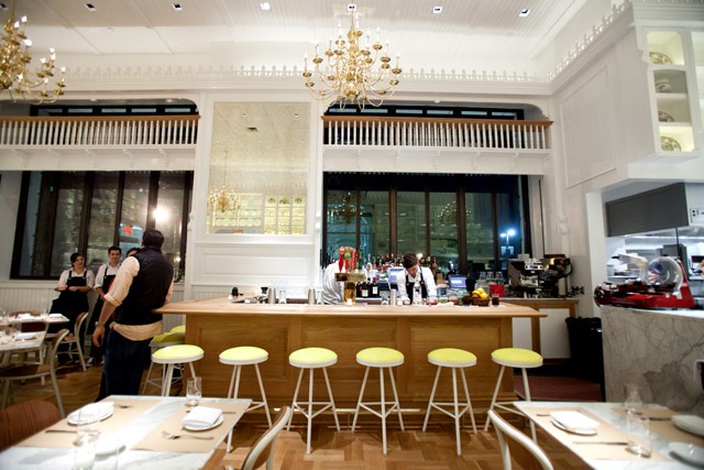 Caffè Storico — marble-topped bar with yellow stools and lit brass chandeliers in evening light