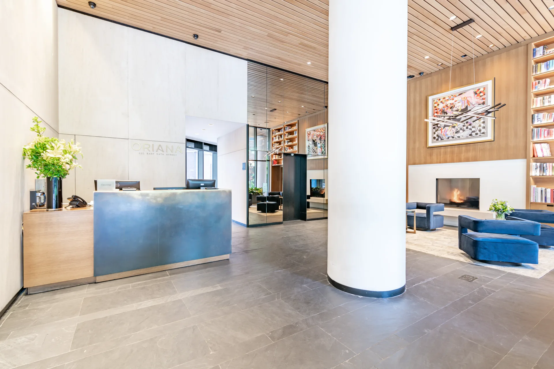 The Oriana — lobby reception with ORIANA signage, perforated screen, and fireplace lounge beyond